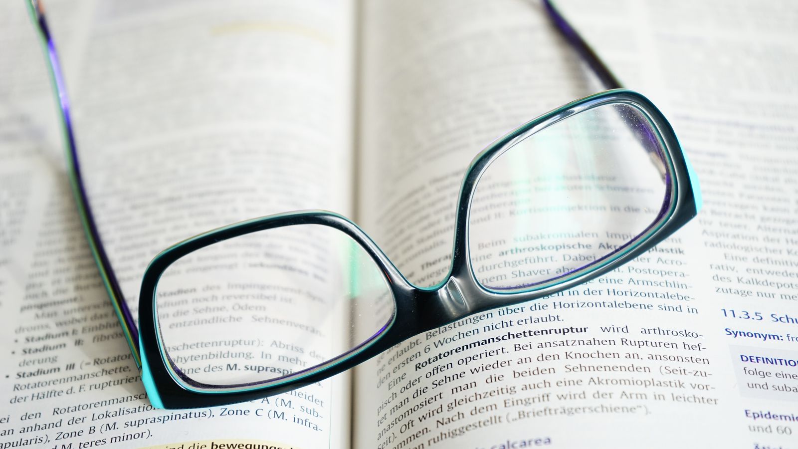 Pair of reading glasses resting on an open book beside a home health kit