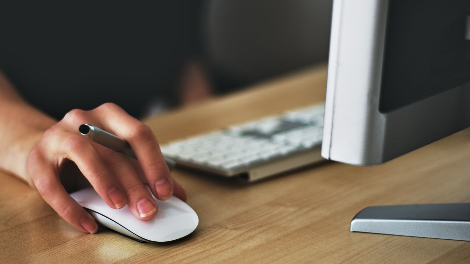 Person using an ergonomic pen mouse and keyboard on a desk setup