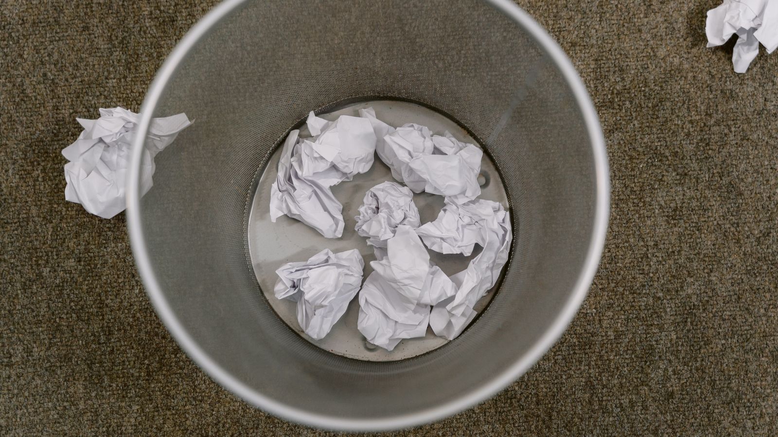 Cross cut shredder sitting under an office desk with shredded paper strips inside the bin