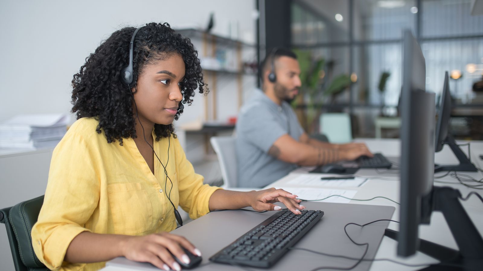 Call center agent working at a compact ergonomic desk with headset and dual monitors