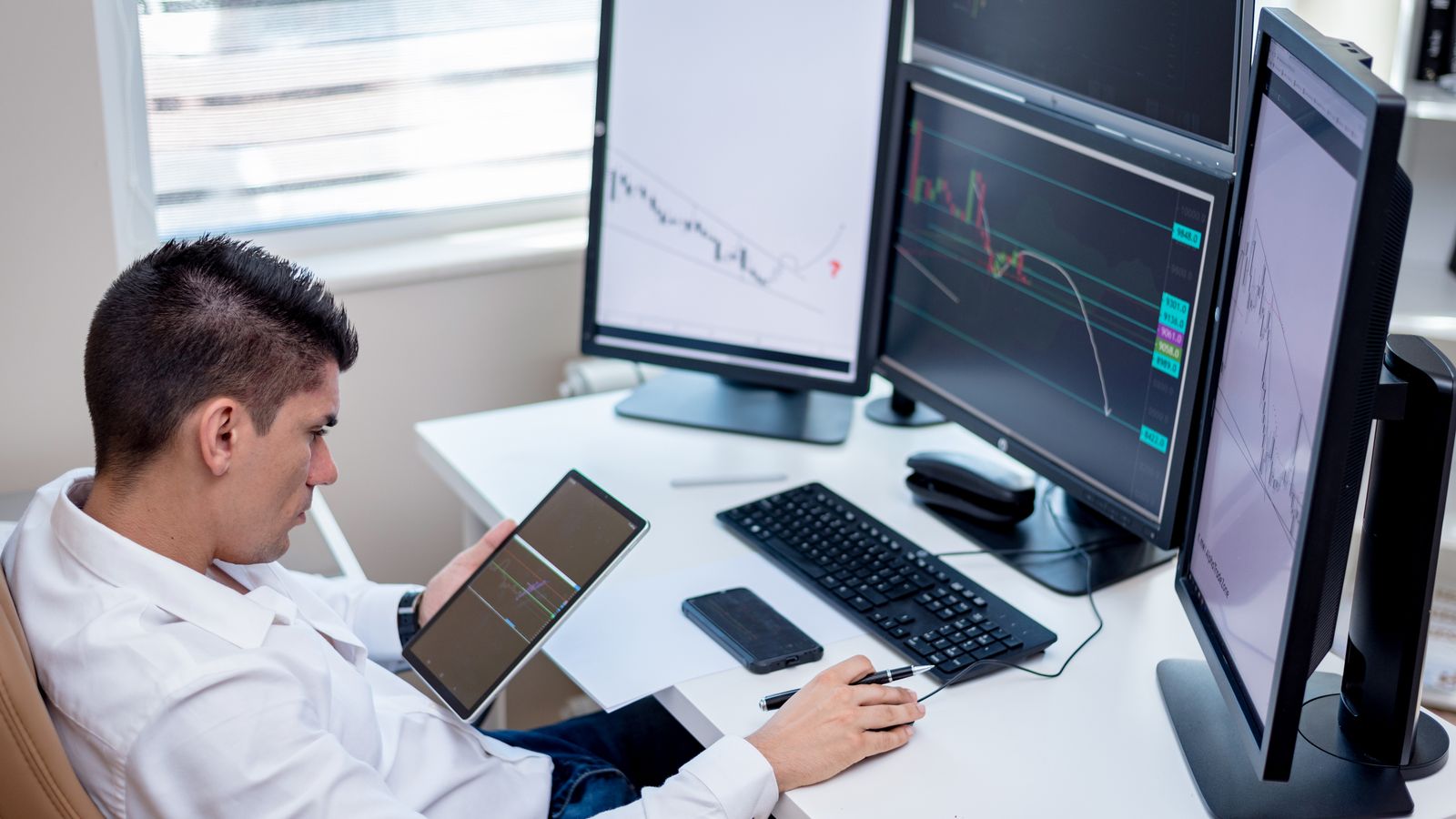 Trader desk setup with multiple monitors displaying stock charts and financial data