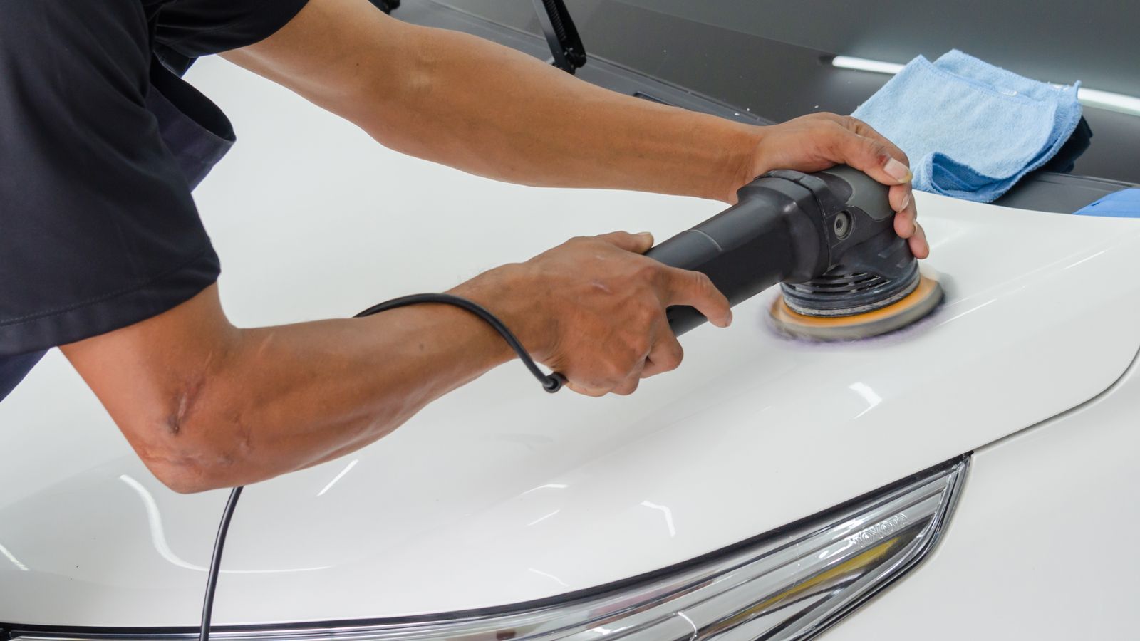 Person applying car wax by hand to a vehicle's hood with an applicator pad