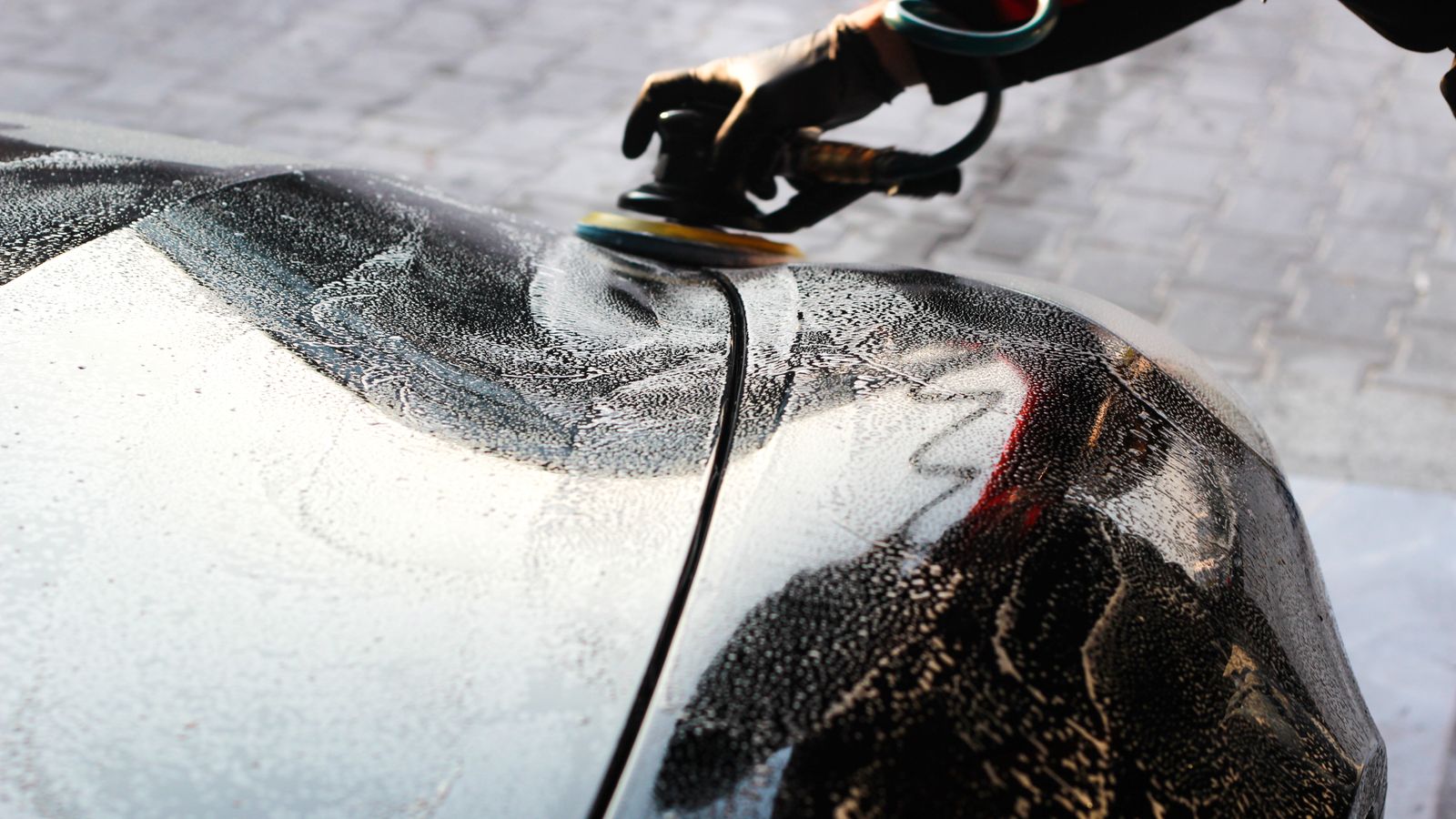 Bottle of car wax and a clean applicator pad set on a car hood ready for use
