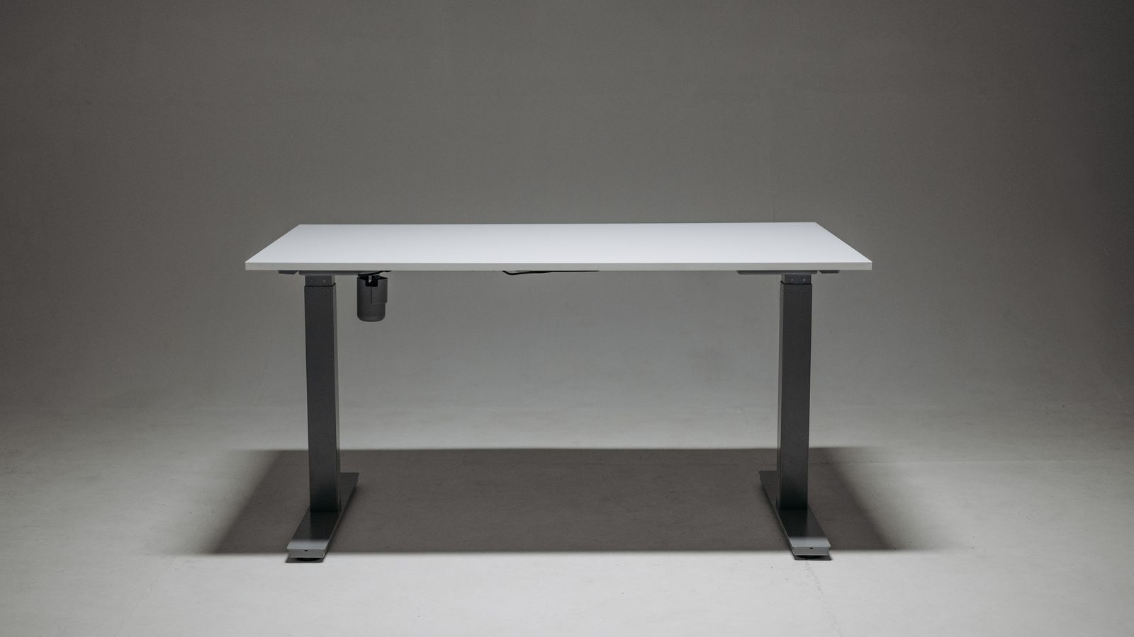 Person kneeling to inspect the telescoping leg column and cables under an adjustable desk